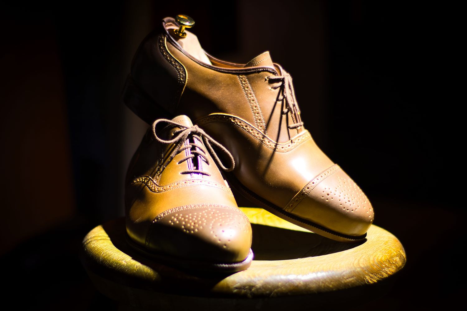 Paar dunkler Herren-Maßschuhe auf dunklem Grund, dramatisch beleuchtet